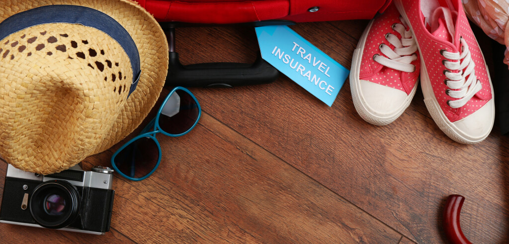 Suitcase and tourist stuff with inscription travel insurance on wooden background