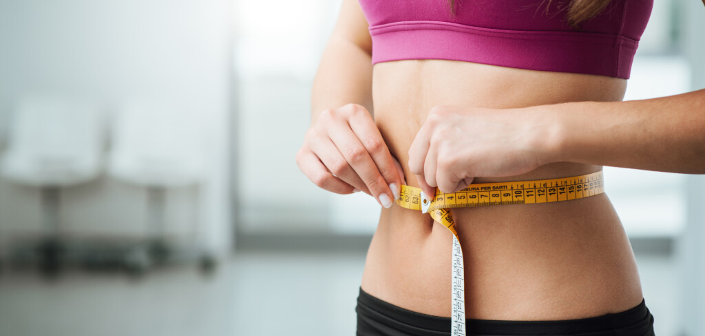 Slim young woman measuring her thin waist with a tape measure, close up