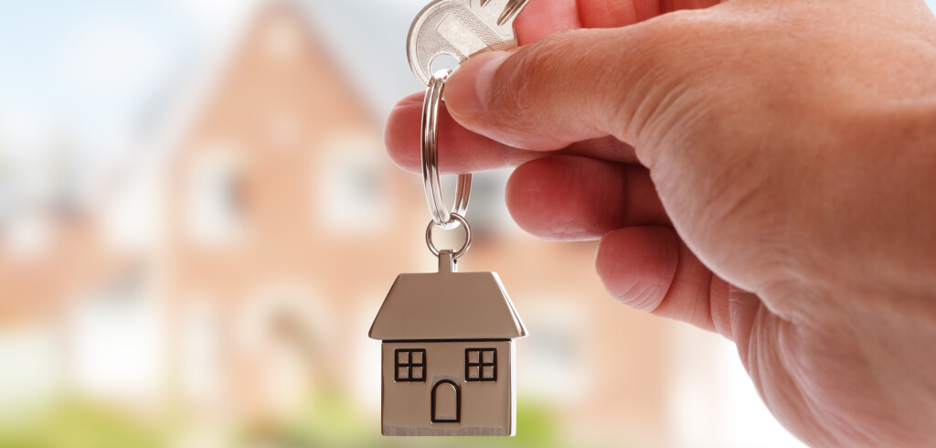 Holding house keys on house shaped keychain in front of a new home