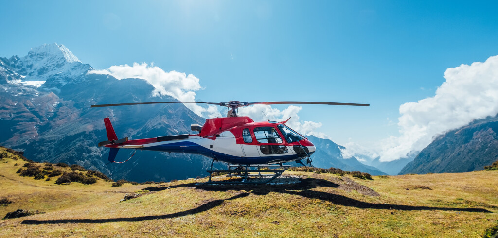 Civil helicopter landed in high altitude Himalayas mountains. Thamserku 6608m mountain on the background. Namche Bazaar, Nepal. Safety air transportation and travel insurance concept image.