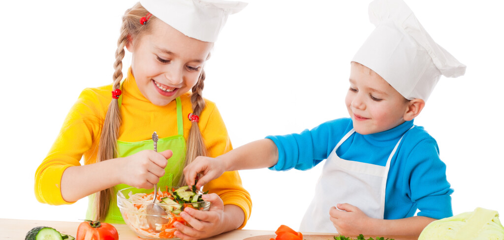 Two smiling kids mixing salad, isolated on white