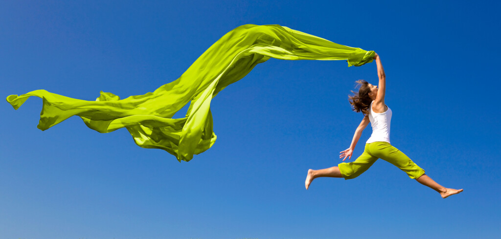 Beautiful young woman jumping on a green meadow with a colored tissue