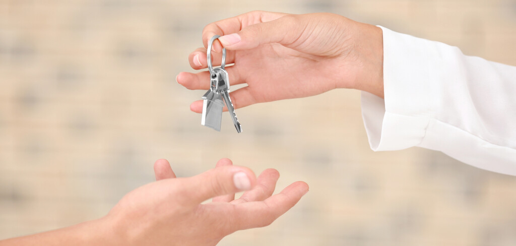 Estate agent giving key from new apartment to man on blurred background