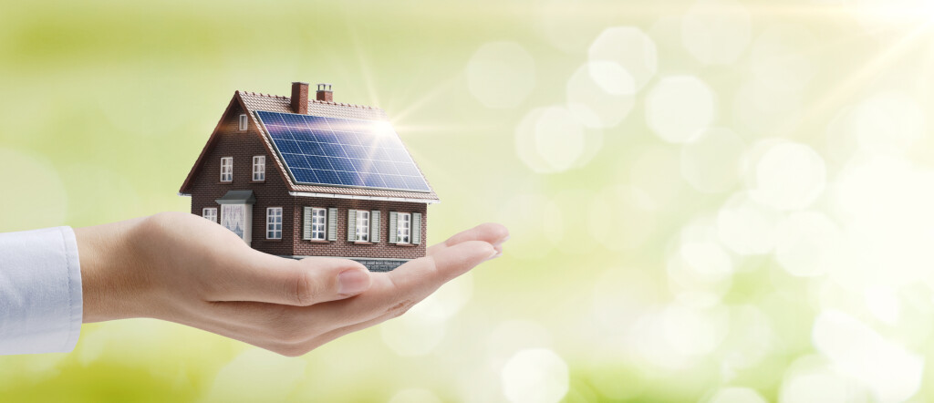 Hand holding an energy efficient model house with solar panels, ecology and sustainability concept