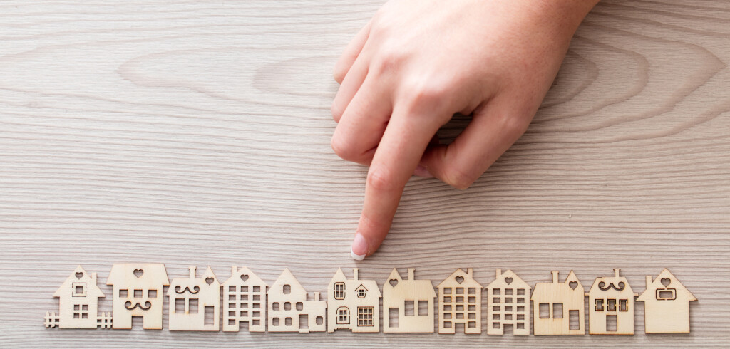 real hand pointing out a house model among the others mini figures in a micro wooden village set