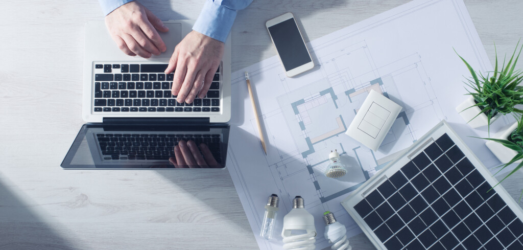 Man working at his desk on a laptop with energy saving CFL lamps, a solar panel and a house project, top view