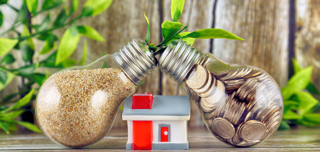 Coins inside the light bulb, plant growing inside the light bulb and miniature house. Green eco renewable energy concept. Electricity prices, energy saving in the household.