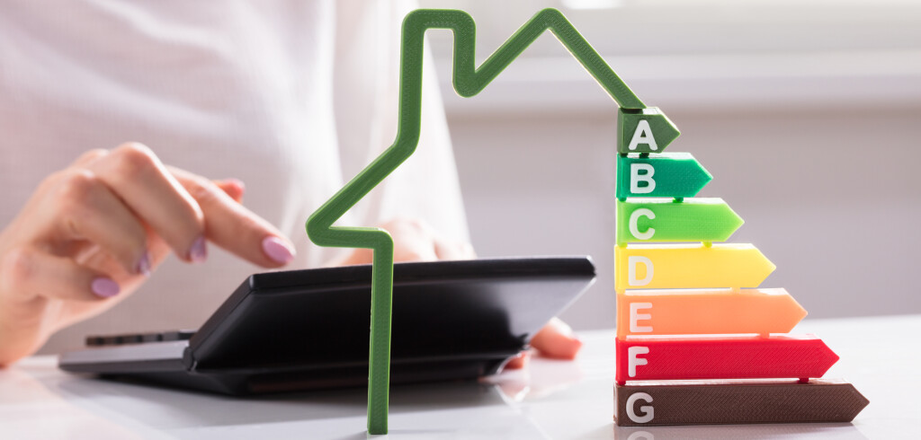 Close-up Of A House Showing Energy Efficiency Rate In Front Of Businesswoman Using Calculator