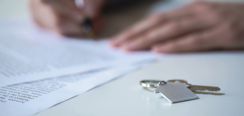 Person signing real estate purchase agreement, key from apartment on table