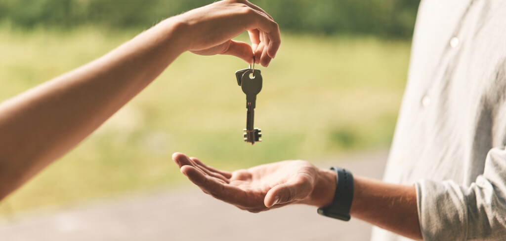 Close up of female real estate agent giving keys to man. Young man buying first country house, purchasing property or becoming homeowner, renting apartment or getting lease or mortgage investment