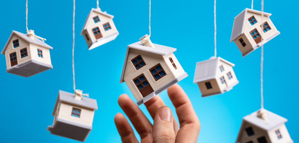 Person's Hand Holding Hanging Model House Against Blue Background