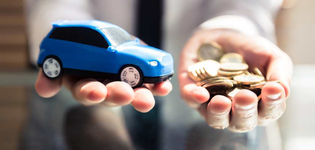 Close-up Of A Businessperson's Hand Holding Small Blue Car And Golden Coins