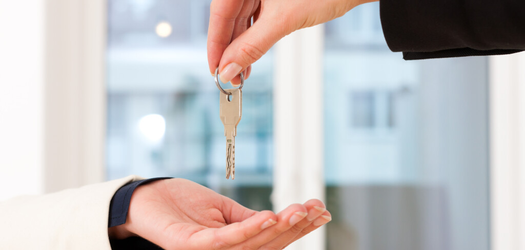 Young realtor is giving the keys to an apartment to the tenant, close-up on keys and hands